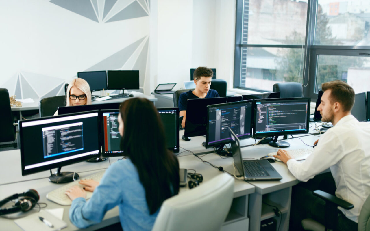 Vier Entwickler sitzen im Büro vor ihren Rechnern und arbeiten
