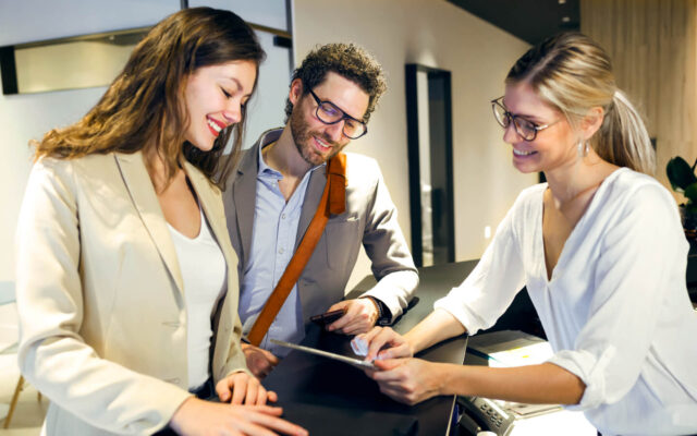 Hotelmitarbeiterin erklärt ankommenden Hotelgästen das Check-In Tablet