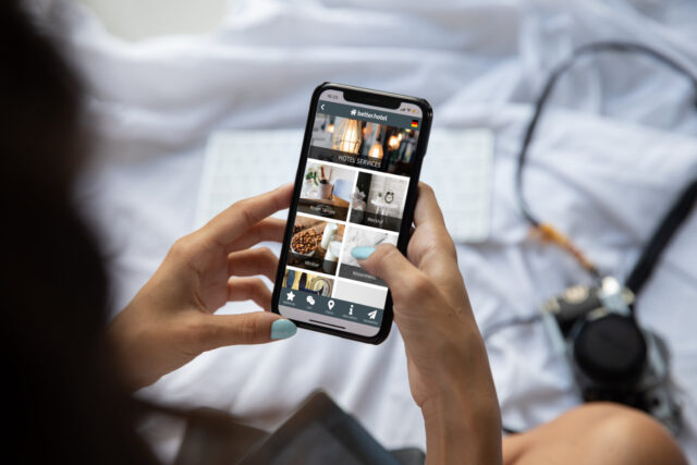 frau hält im hotelzimmer smartphone mit hotel app mit der hand fest