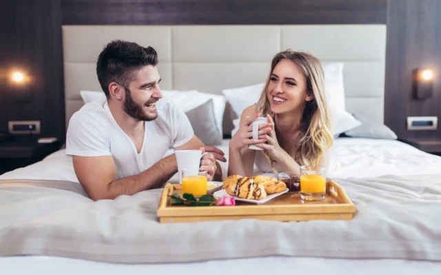 Mann und Frau liegen glücklich im hotel bett und frühstücken