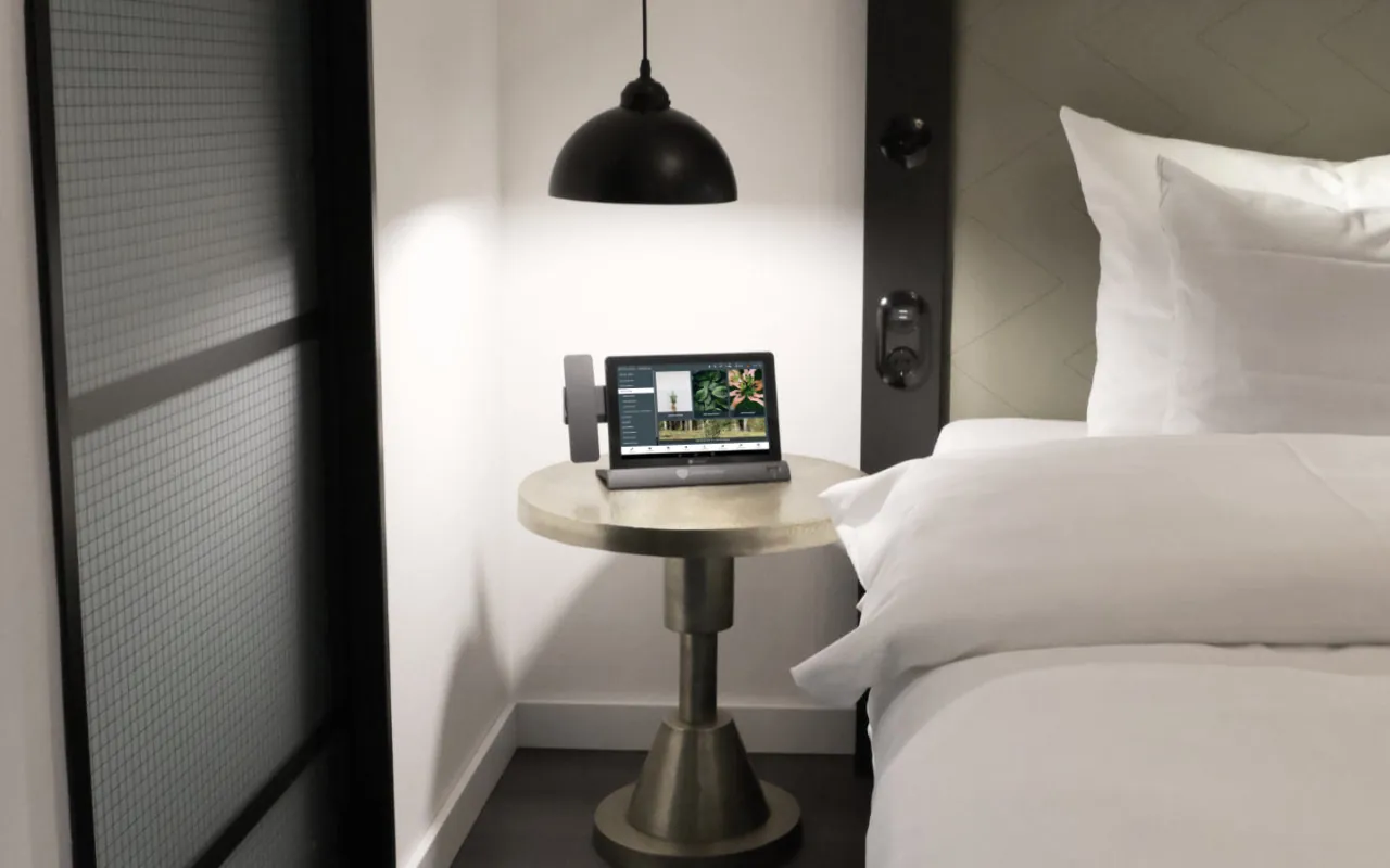 Digitale Gästemappe auf dem In-Room Tablet steht auf Tisch neben Bett im Hotelzimmer