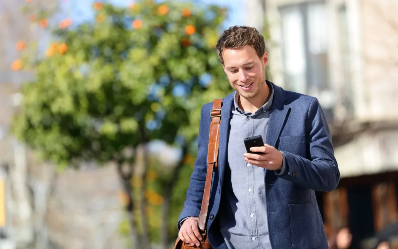 Glücklicher Mann nutzt sein Smartphone beim Spazierengehen