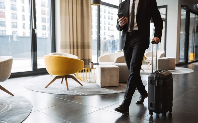 Geschäftsmann mit Smartphone und Koffer läuft durch die Hotellobby