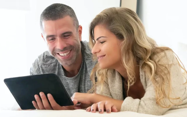 Zwei Hotelgäste liegen im Bett und schauen auf das In-Room Tablet mit digitaler Gästemappe