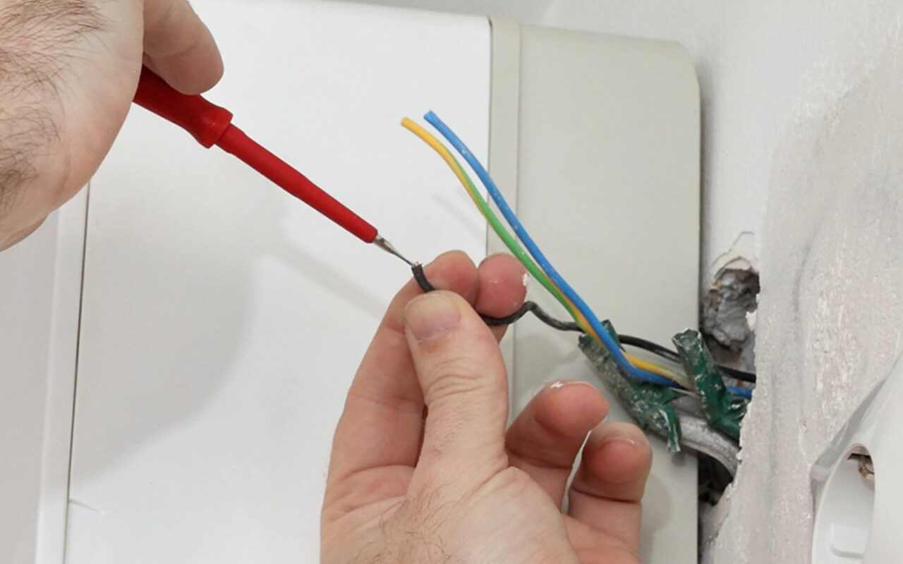 Elektriker handiert mit Kabeln aus der Wand für Fan Coil Wandthermostat Installation